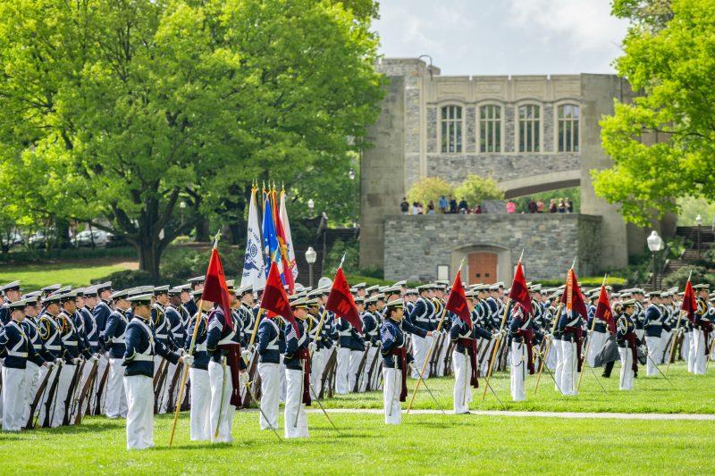 The cadet regiment stands on the Drillfield in dress uniforms. The Pylons and War Memorial Chapel are in the background.